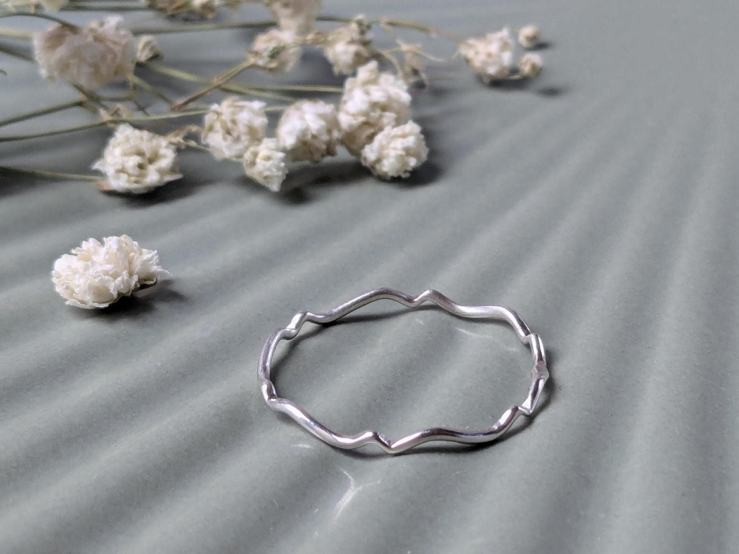 A delicate sterling silver ring with a scalloped wave pattern.