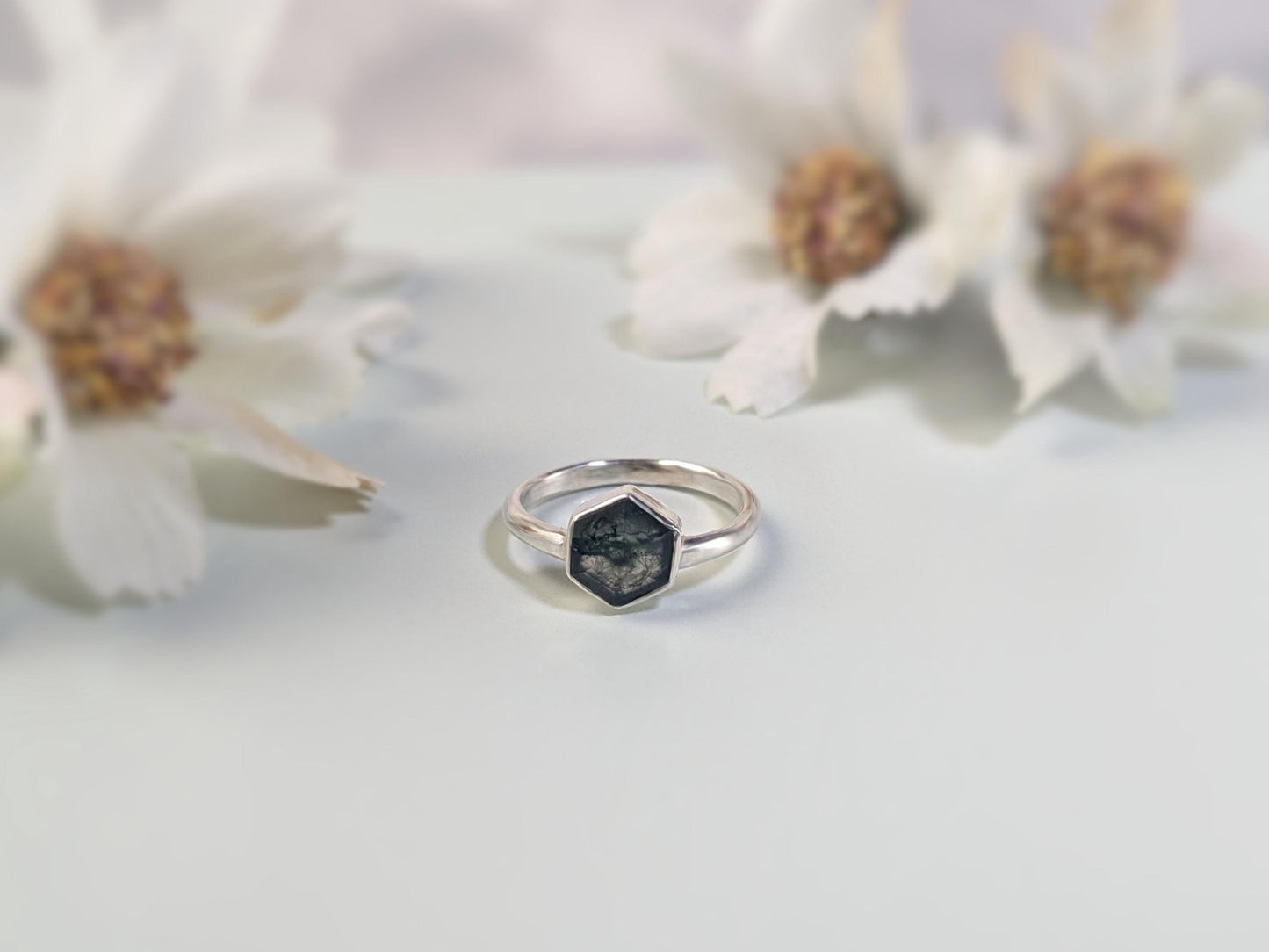 An frontal view of a ring. The ring is made from sterling silver. The ring has a plain band and a hexagon-shaped bezel. The bezel holds a faceted moss agate.