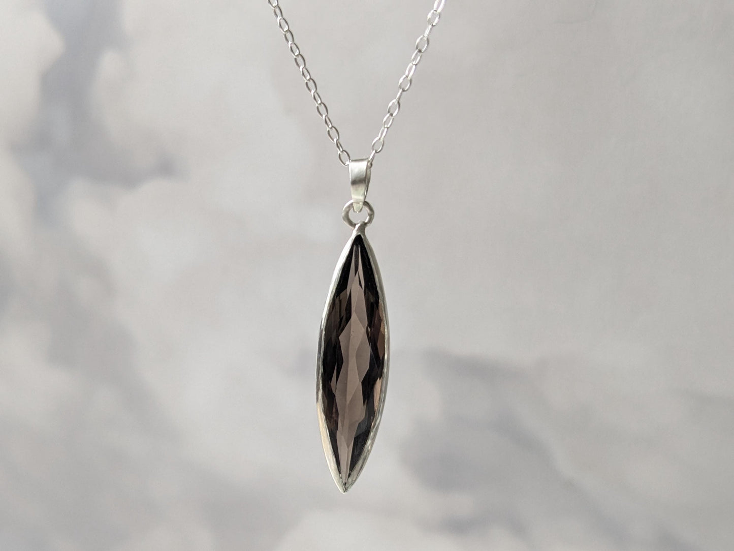 An elegant sterling silver pendant on a simple chain. The pendant is made of an elongated and slender marquise-shaped smoky quartz in a delicate bezel.