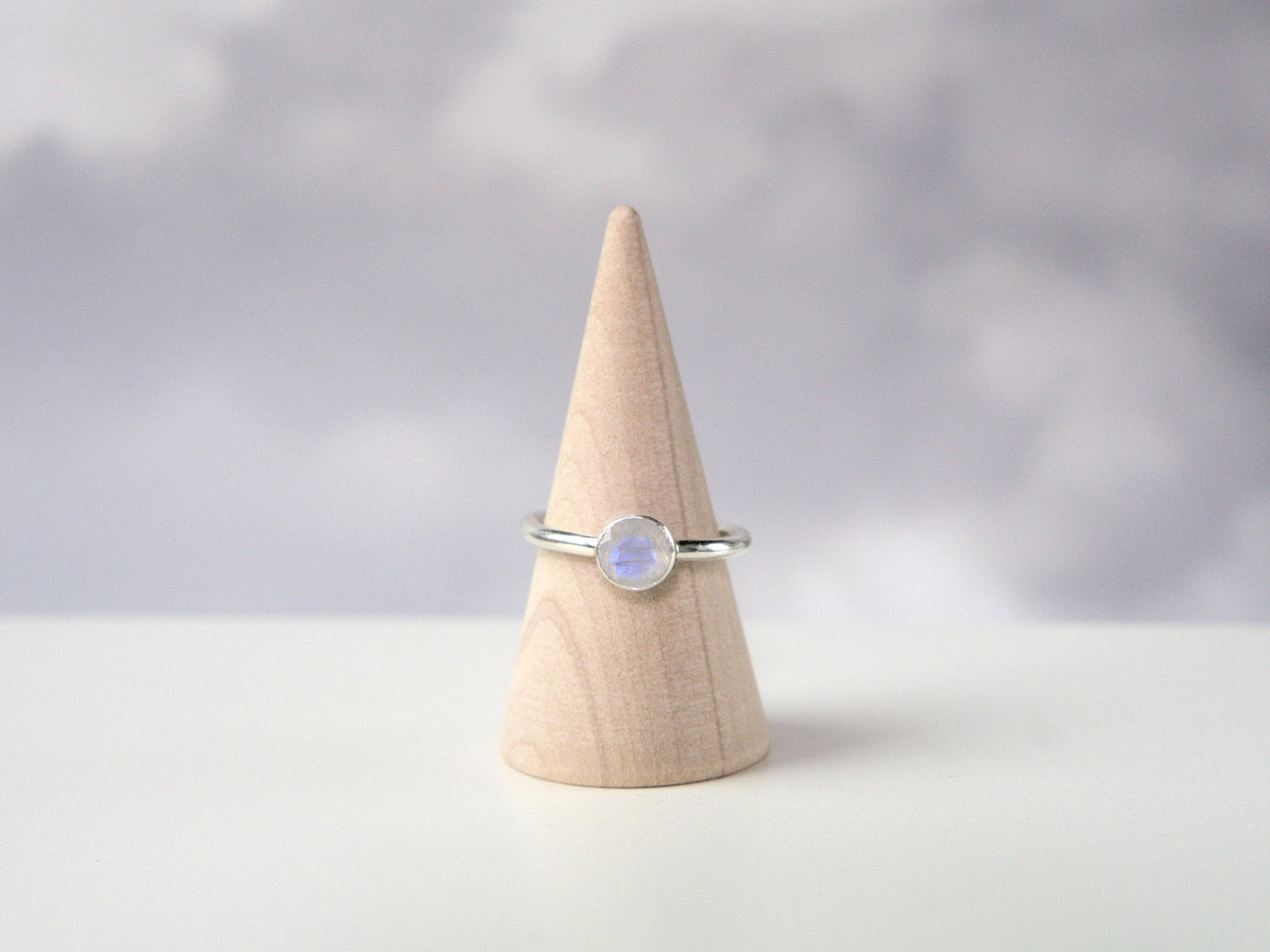 A frontal view of a ring. The ring has a plain sterling silver band with a round bezel. The bezel holds a faceted moonstone.