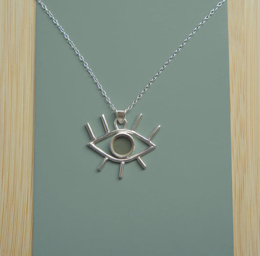 An eye-shaped pendant sitting on a simple chain. The pendant is mader from sterling silver and has eyelashes made of silver wire and an iris made of smokey quartz. 