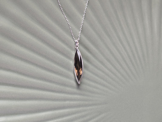 An elegant sterling silver pendant on a simple chain. The pendant is made of an elongated and slender marquise-shaped smoky quartz in a delicate bezel. 